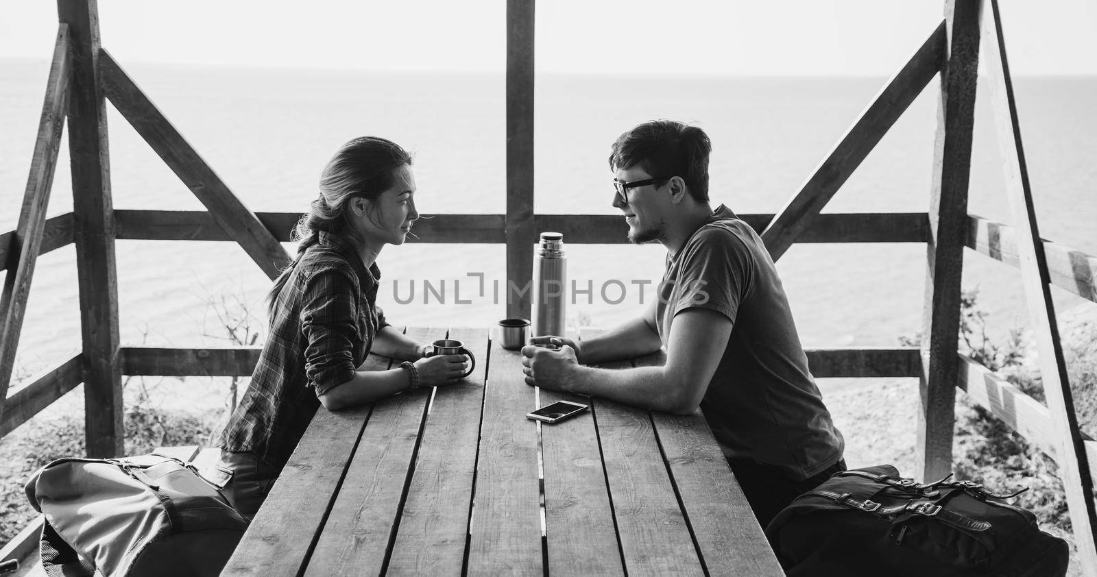 Young loving couple resting in wooden terrace and talking with each other in summer outdoor. Monochrome image