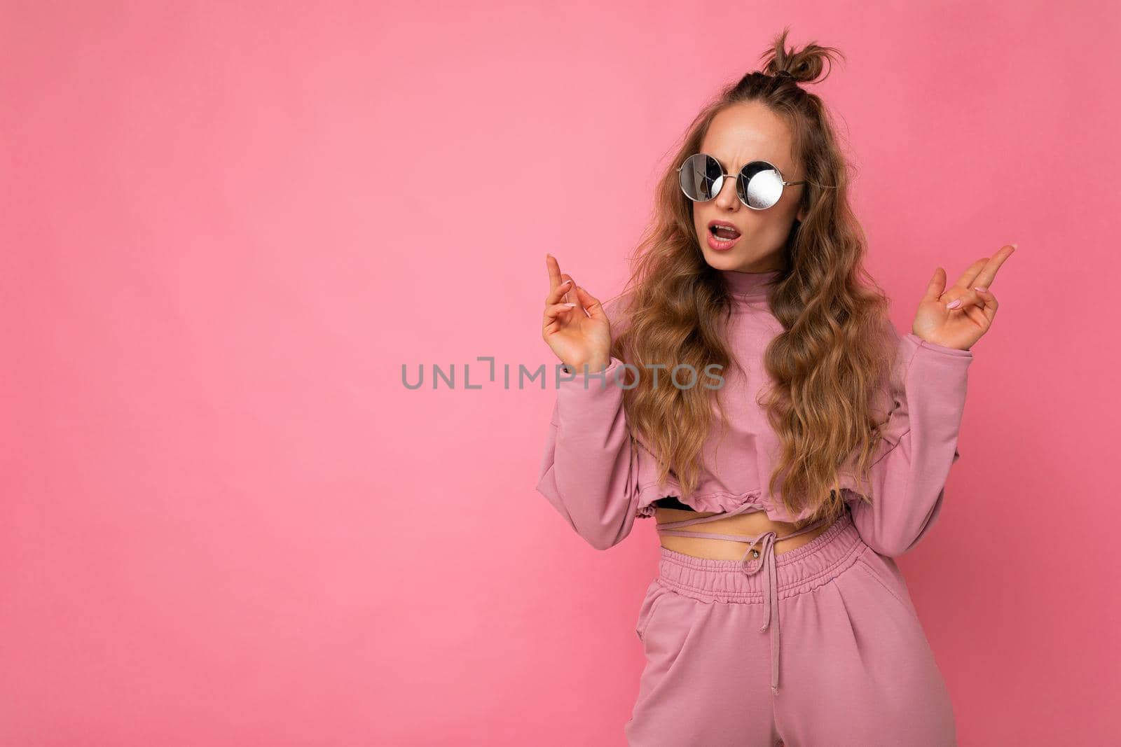 Attractive sexy self-confident young blonde woman wearing everyday stylish clothes and modern sunglasses isolated on colorful background wall looking to the side. copy space