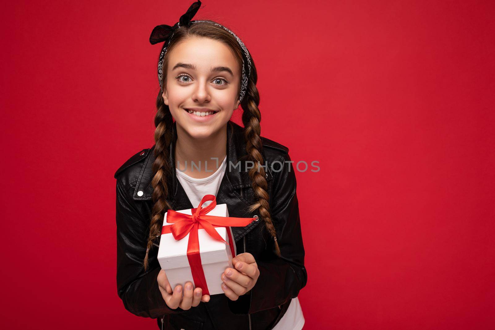 Beautiful happy brunette girl isolated over colourful background wall wearing stylish casual clothes holding gift box and looking at camera.