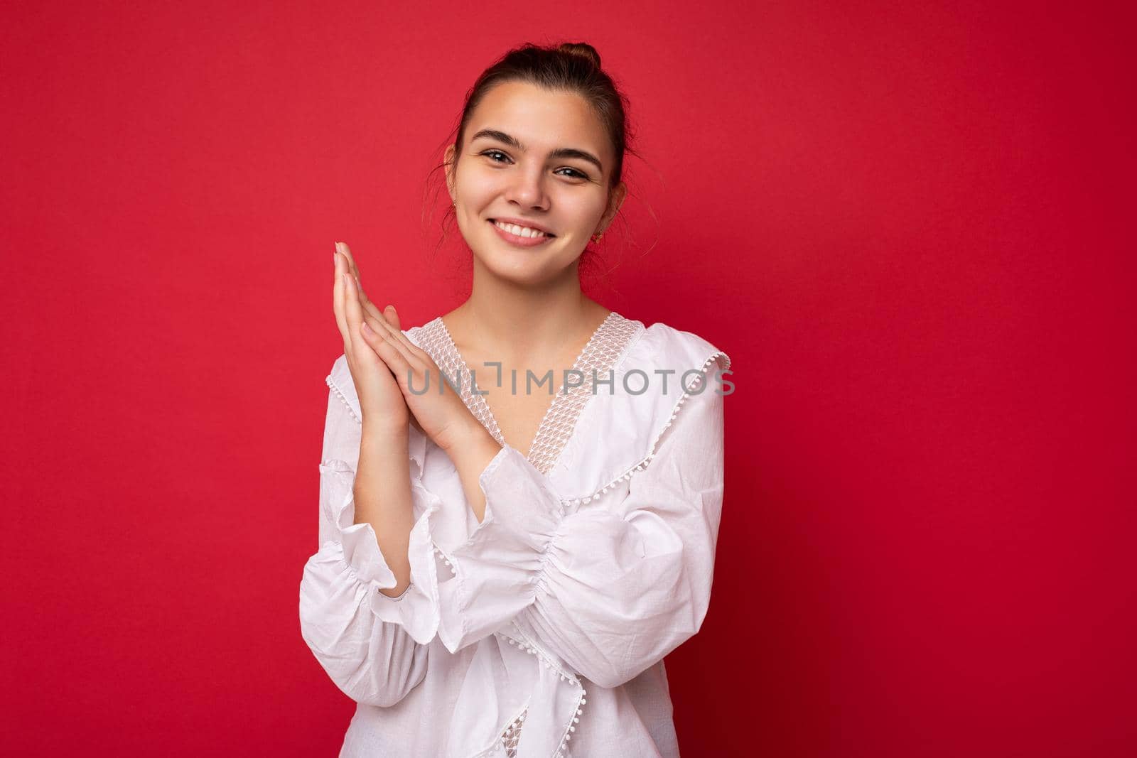 Young beautiful european stylish brunette woman wearing white blouse isolated over red background with positive sincere emotions. Simple and natural looking at the camera. Free space.