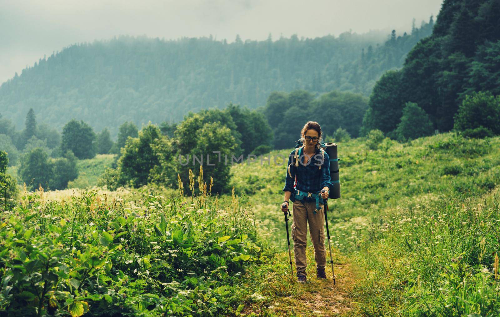 Explorer young woman with trekking poles walking in summer mountains