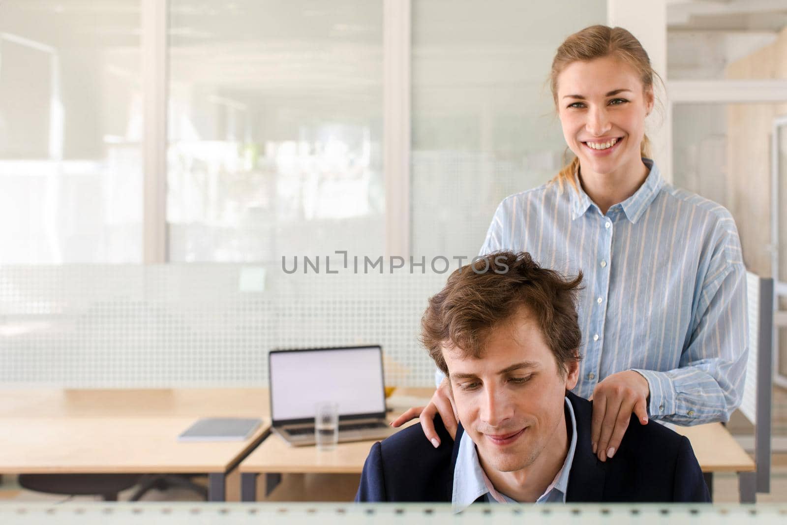 Crop view of attractive smiling female doing neck massage for sitting man in suit on working place