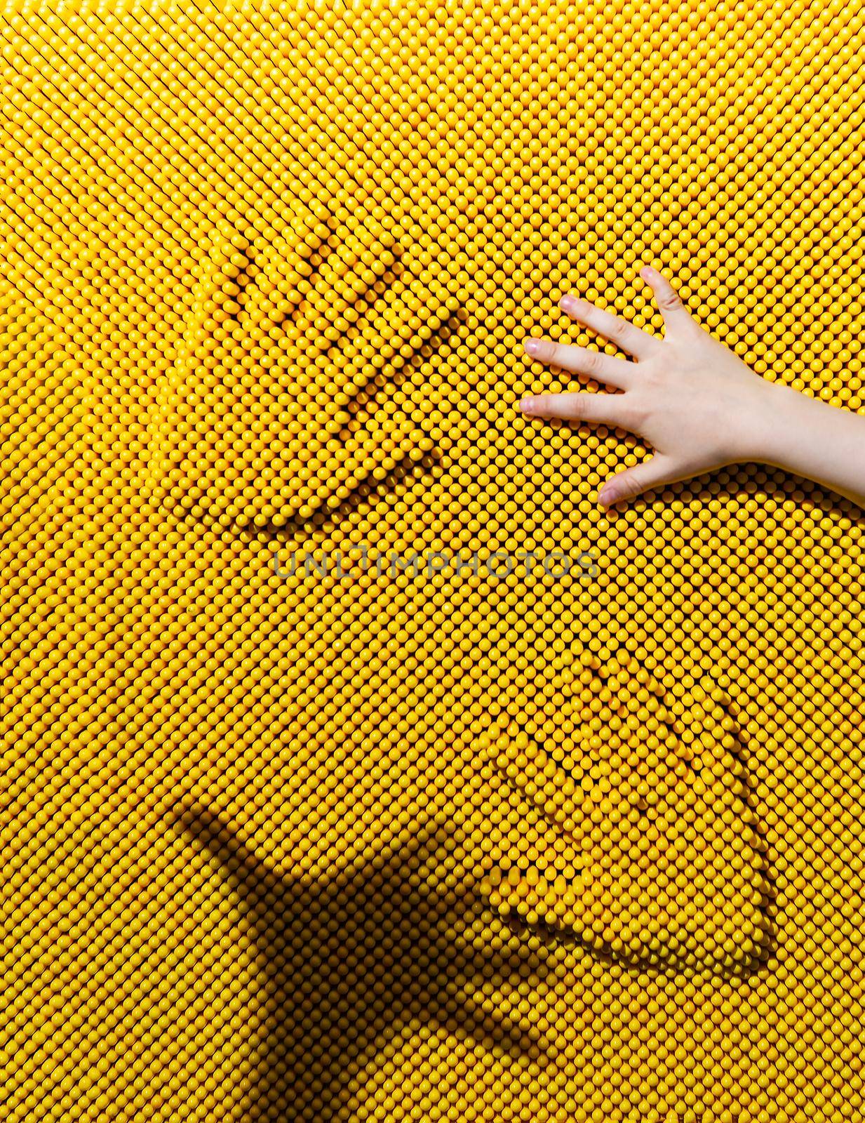 Two handprints on the yellow plastic pinscreen, children's hand and hand shadow. Child playing with contact screen. Pinart