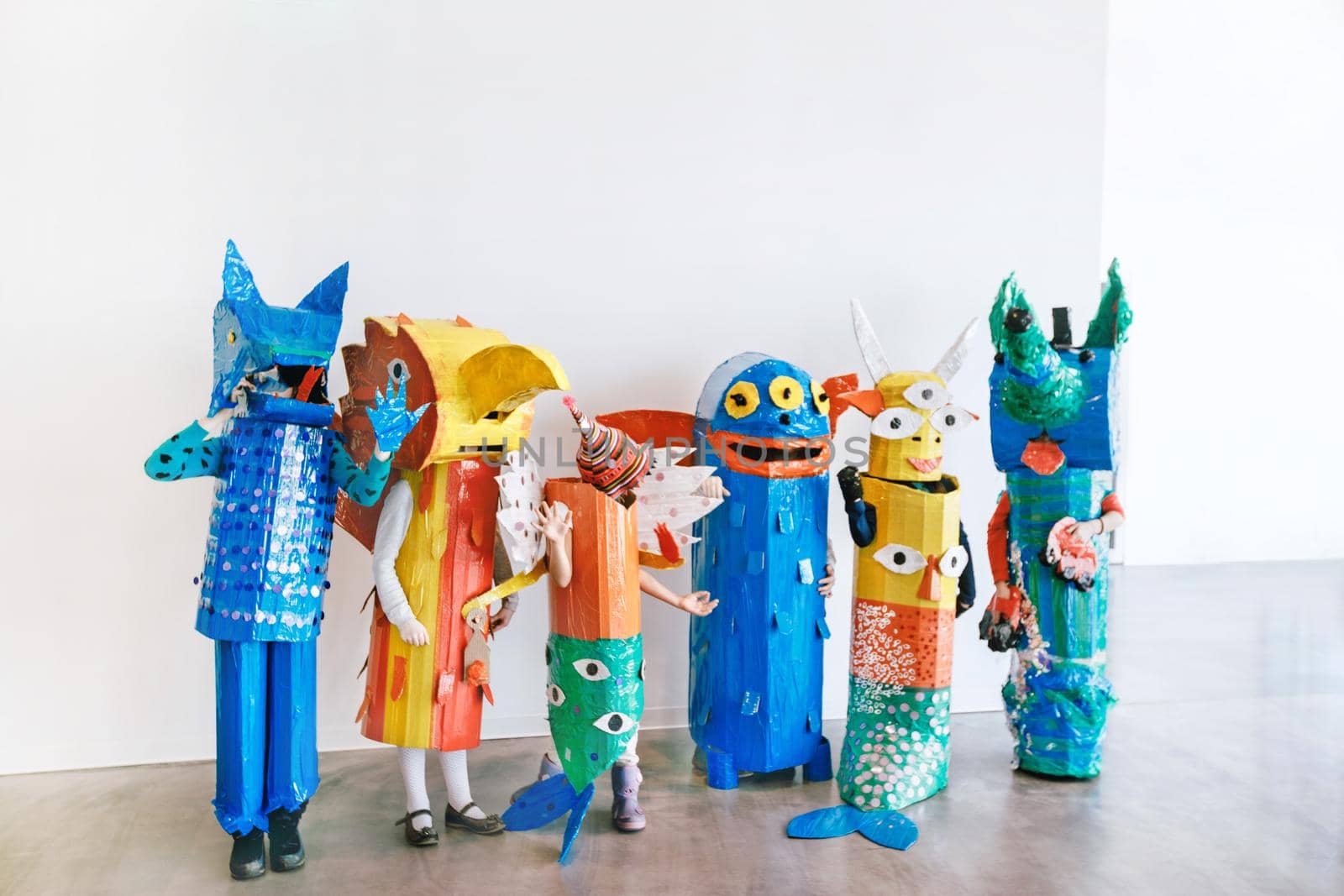 People in handmade colorful monsters costumes standing together in studio.