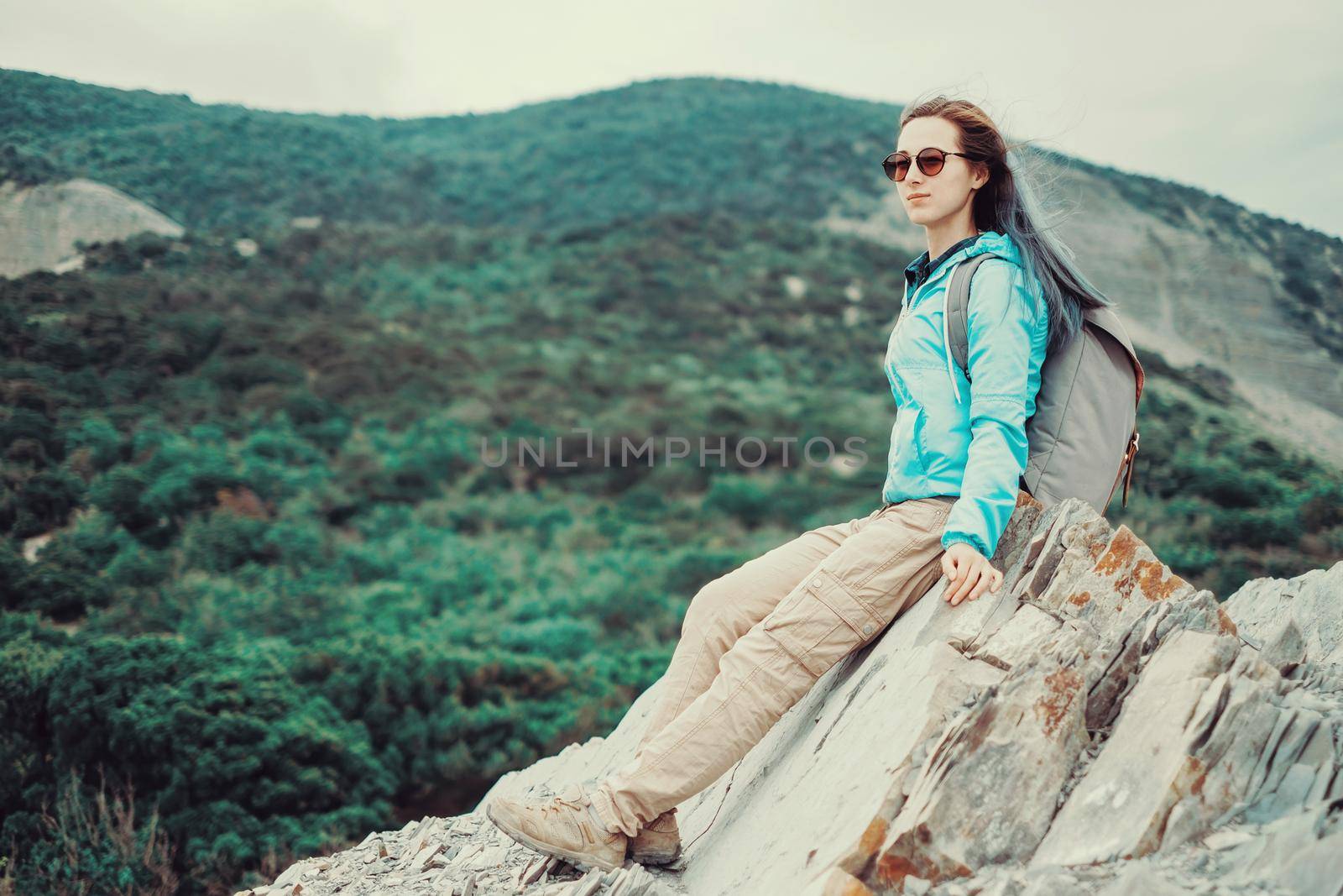 Beautiful hiker young woman resting on rocks in summer mountains. Toned image
