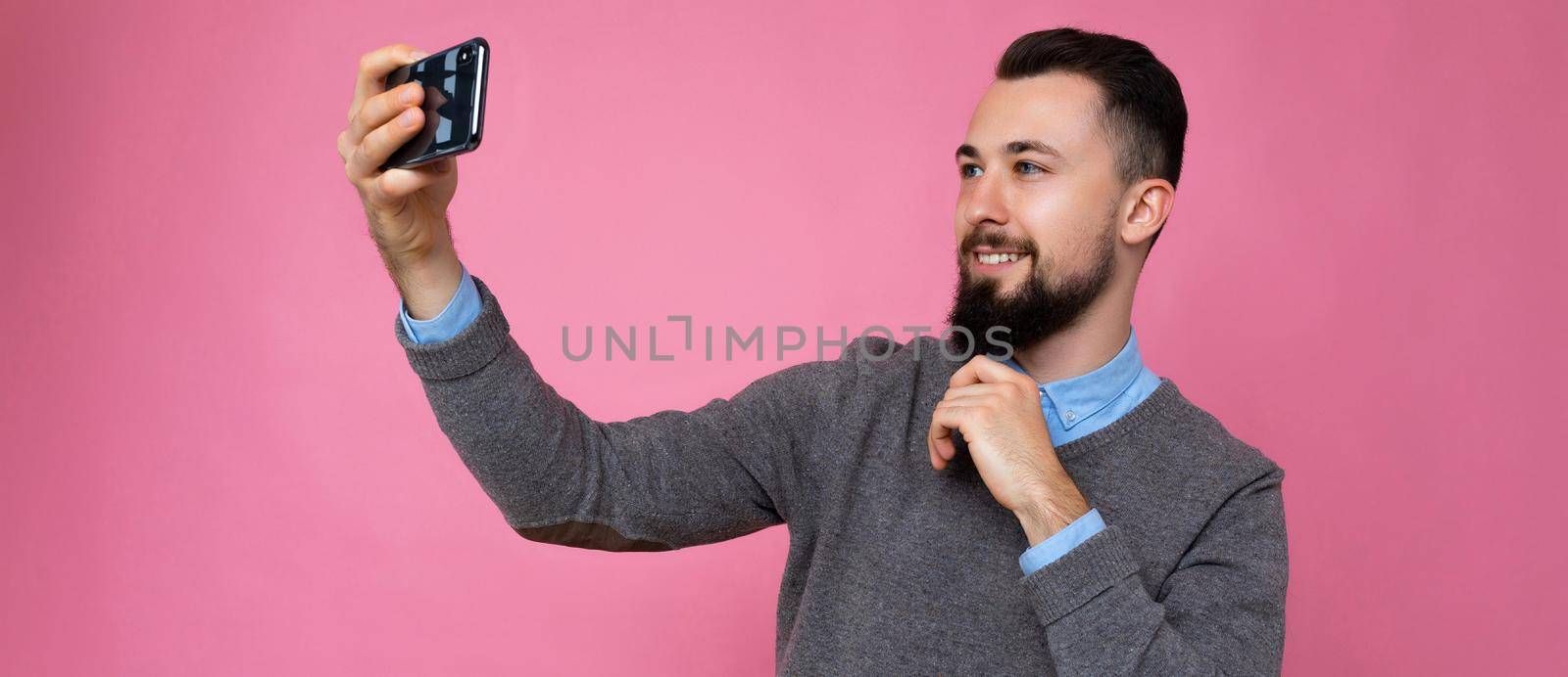 panoramic photo of Handsome young man wearing casual stylish clothes standing isolated over background wall holding smartphone taking selfie photo looking at mobile phone screen display by TRMK