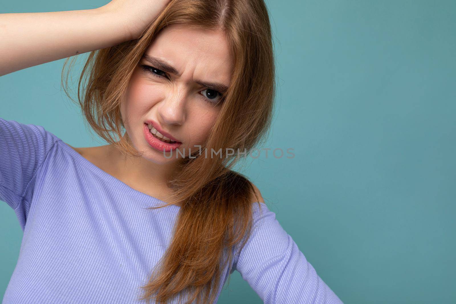 Dissatisfied angry young beautiful dark blonde woman with sincere emotions isolated on background wall with copy space wearing casual blue crop top. Negative concept.