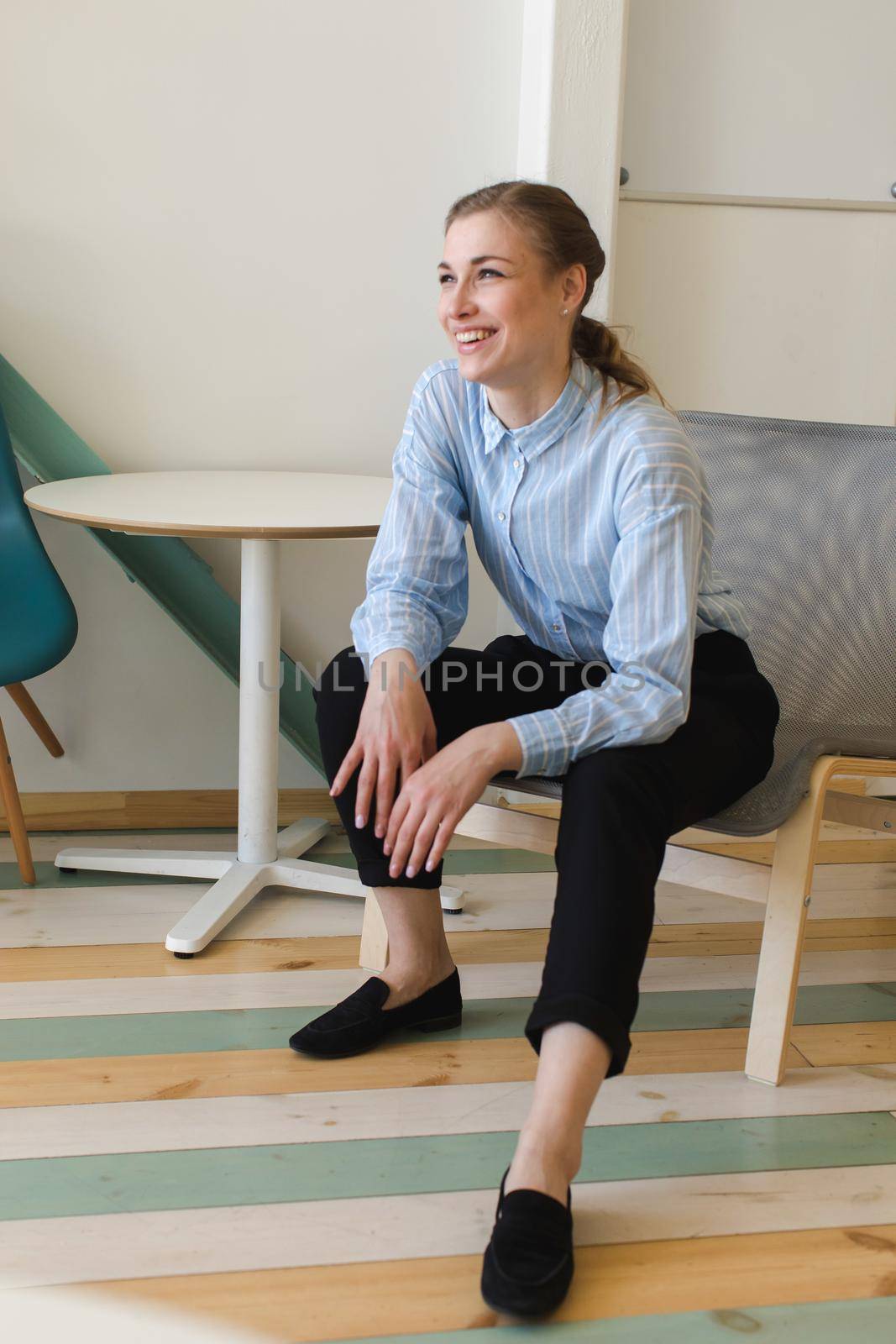 Full body of female worker laughing happily at spare time in modern workplace while looking away
