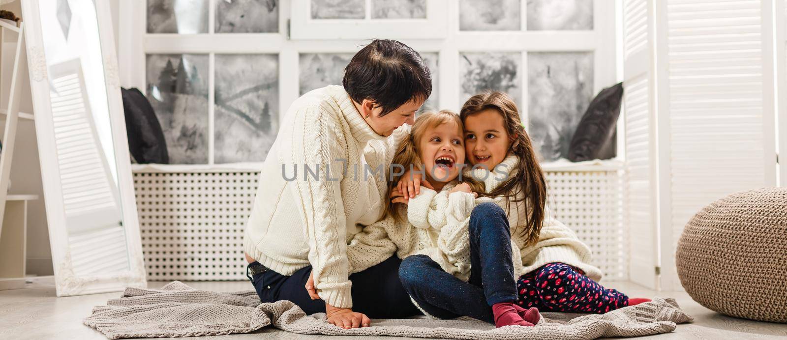 Merry Christmas and Happy Holidays. Cheerful mom and her cute daughters girls exchanging gifts. Parent and two little children having fun and playing together near Christmas tree indoors. by Andelov13