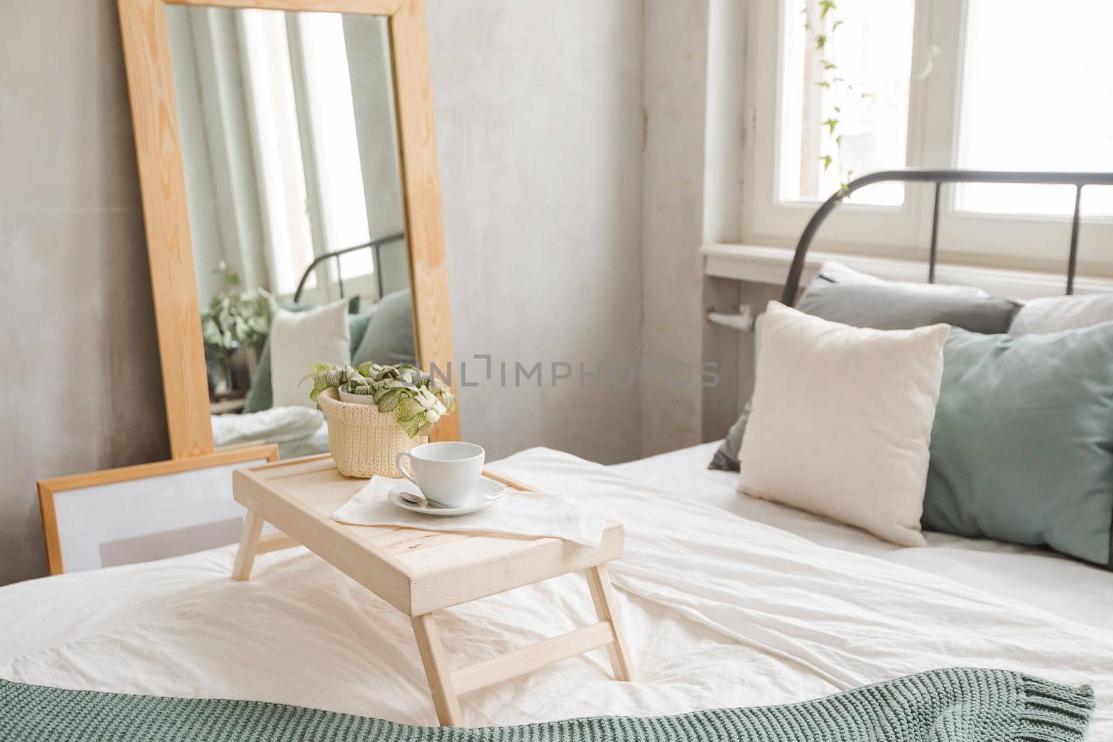 Interior shot of made bed in daylight with wooden table served on top with cup of coffee.