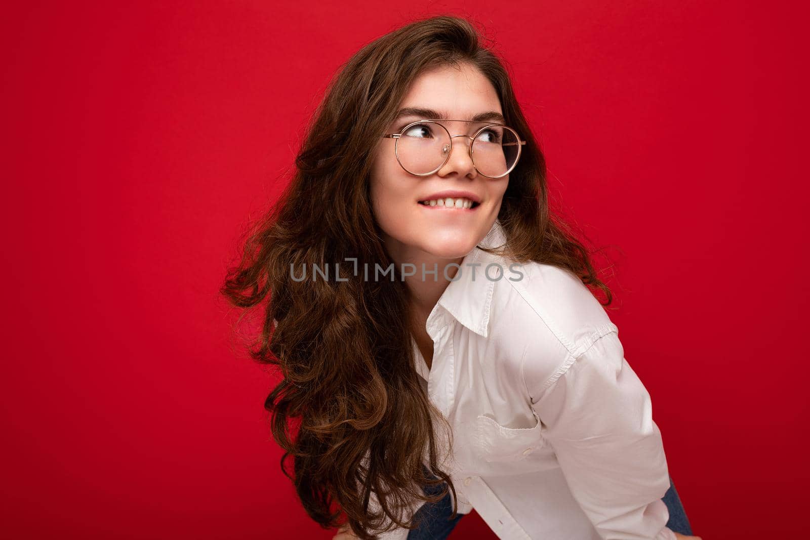 Photo shot of beautiful positive young brunette woman wearing casual clothes and stylish optical glasses isolated over colorful background wall looking to the side.