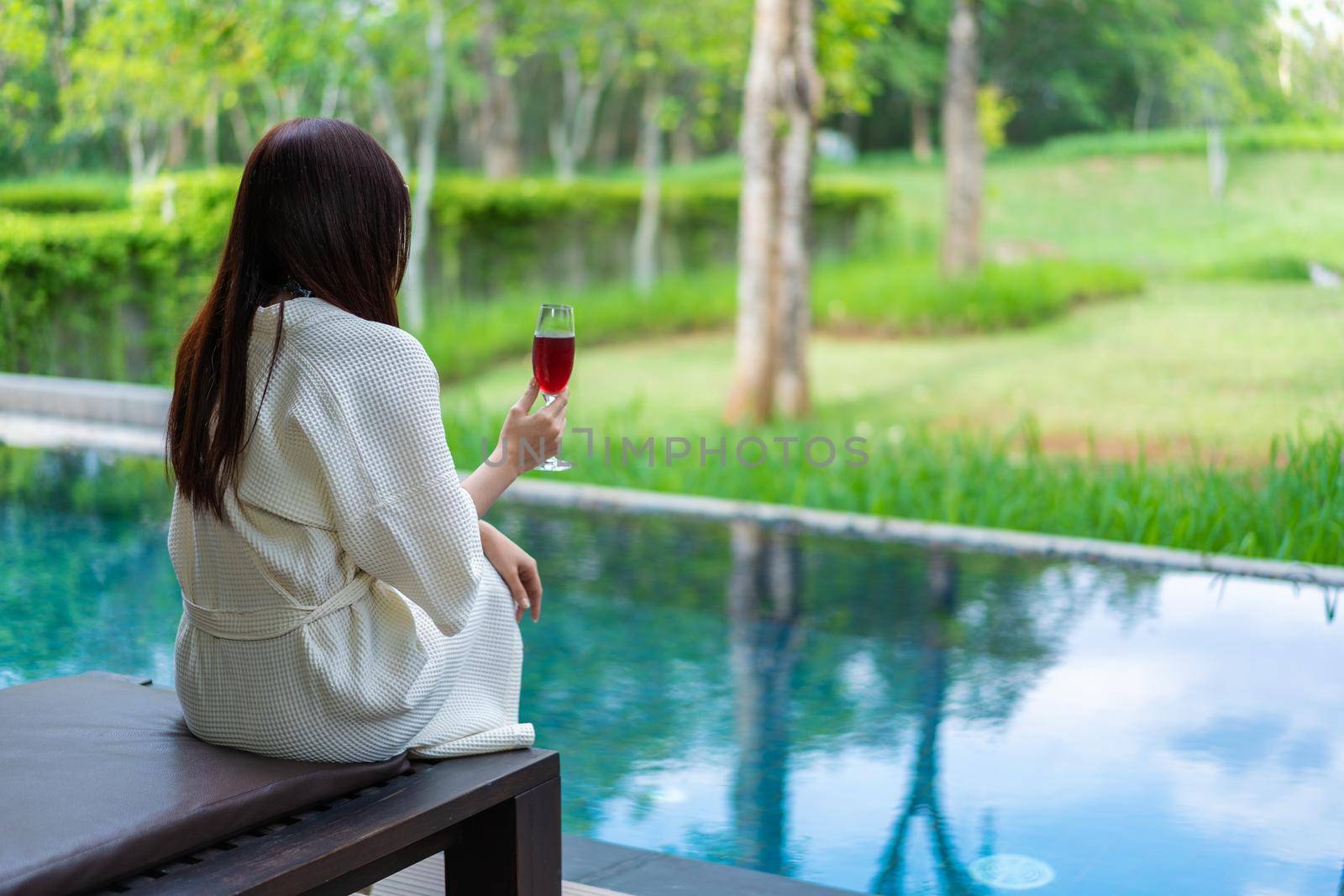 woman clothed bathrobe sitting on deckchair in swimming pool