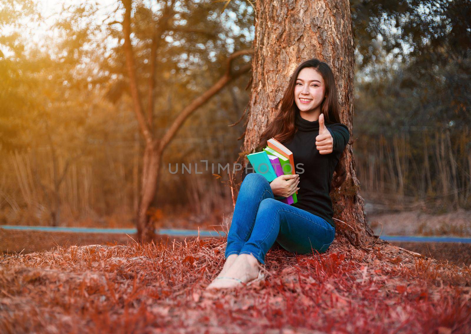 young woman holding a book and showing thumb up sign in the park