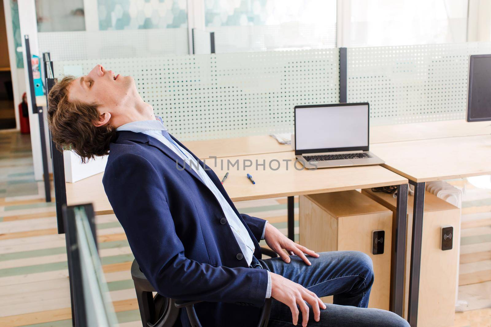Side view of young office employee in formal suit sleeping sitting on chair in office