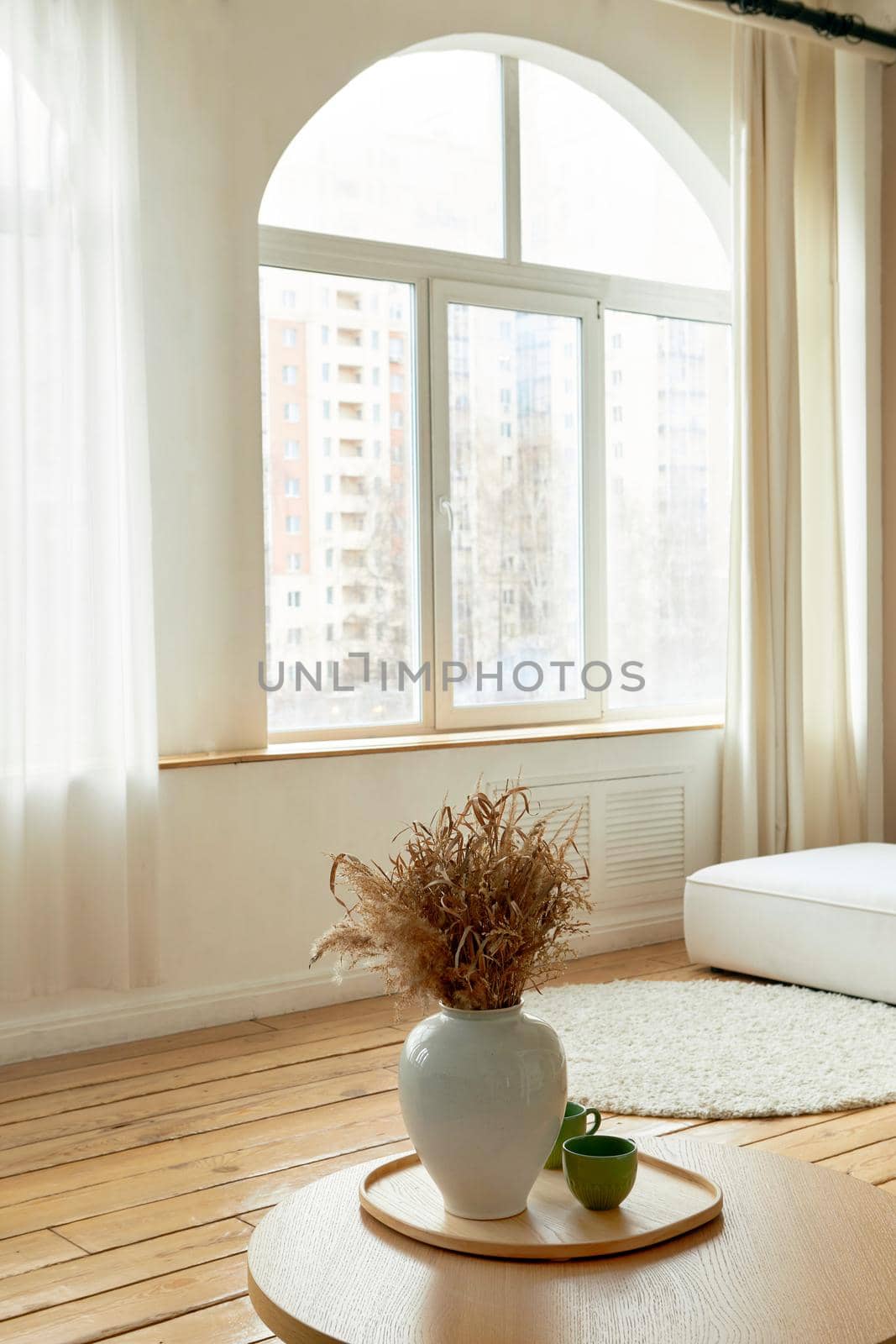 Interior of modern living room decorated with vase of bunch of flowers placed on round shaped wooden table in apartment