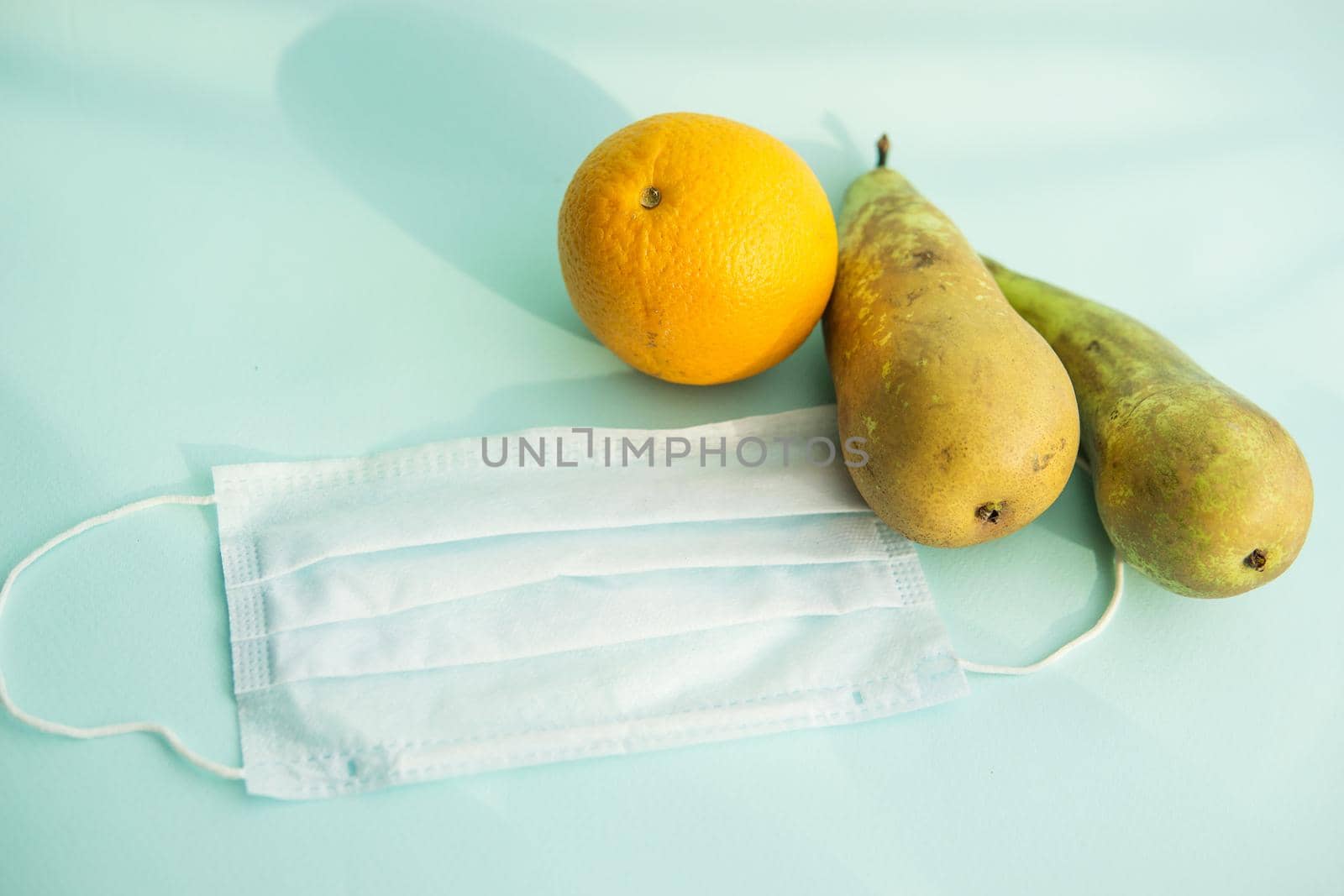 Fruit and protective mask on a mint background, fruit harvest, protection from coronavirus, fruit from China. Close-up, top view.