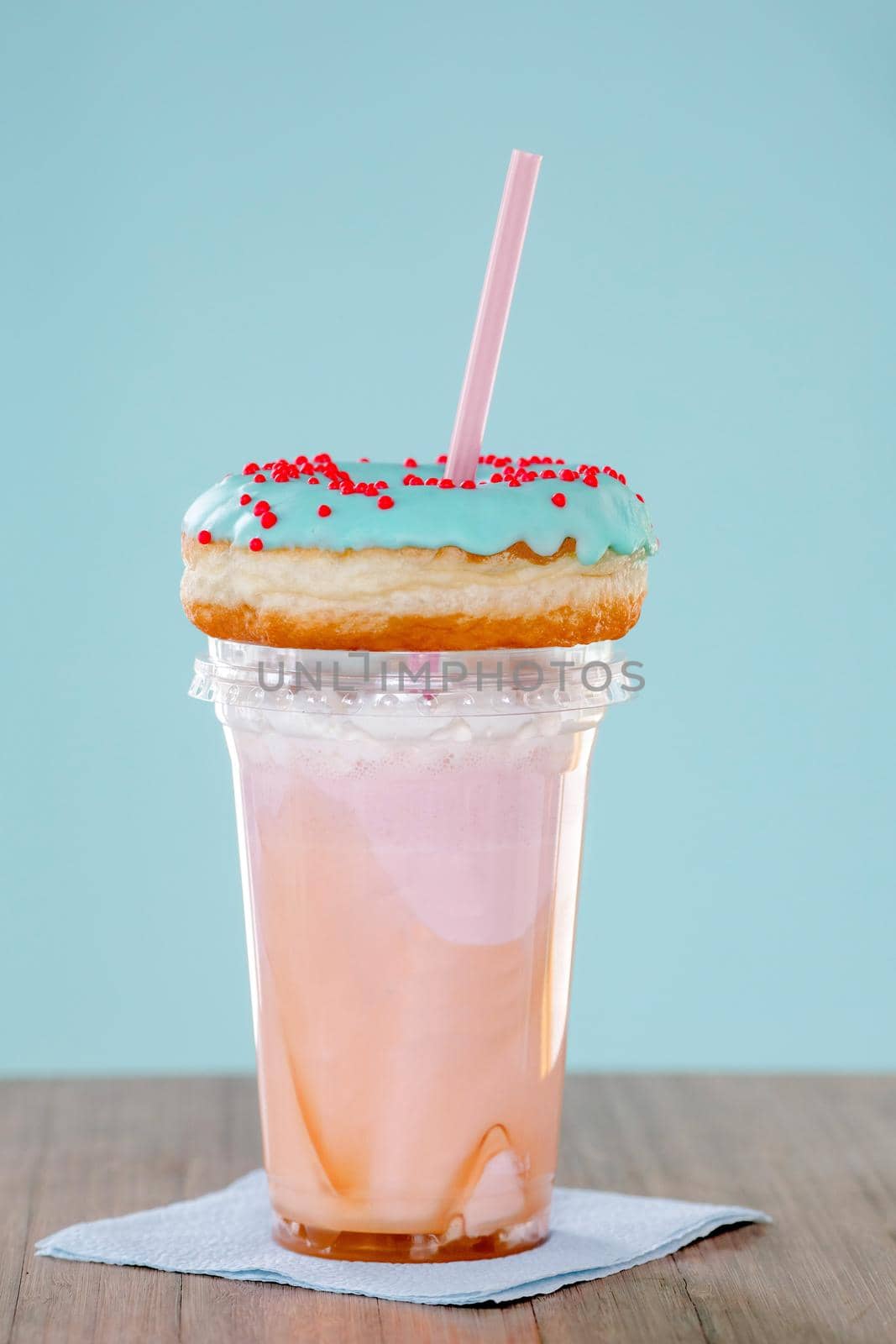 Pink and donuts extreme milkshakein a plastic cup on blue background. Crazy freakshake or overshake on wooden table with copy space