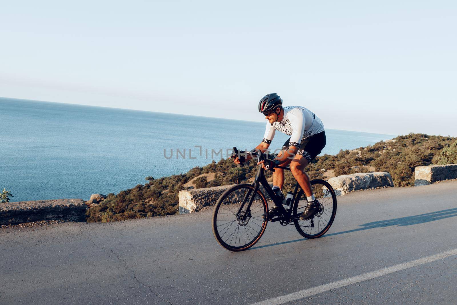Man cyclist pedaling on a road bike outdoors in sun set at coastal road
