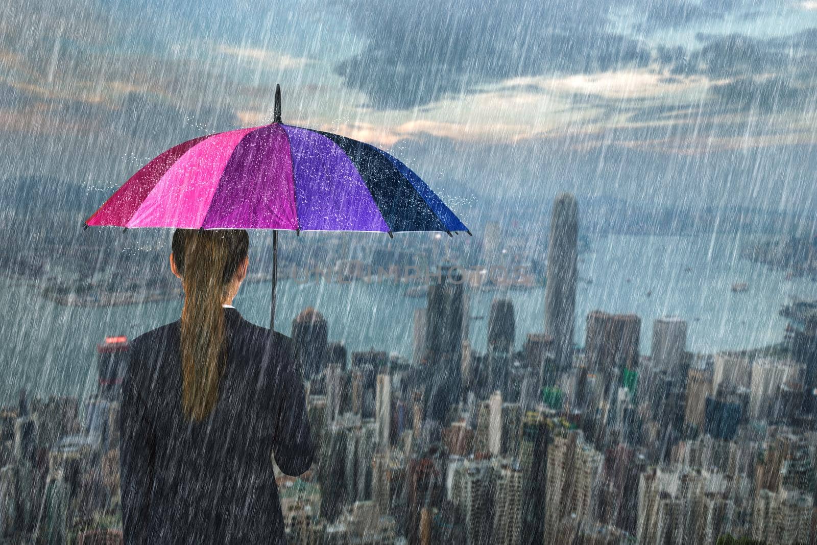 business woman holding multicolored umbrella with falling rain at Hong Kong city background