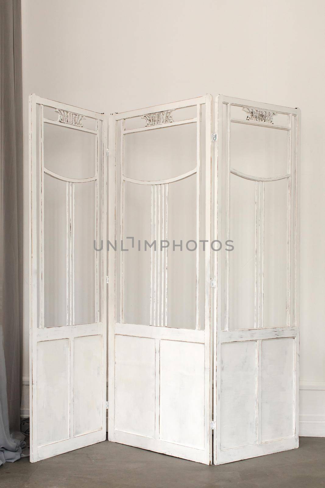White delicate decorative wood panel on white plaster wall. Boudoir wedding room. Retro folding screen. Vintage ornate carved folding screen.