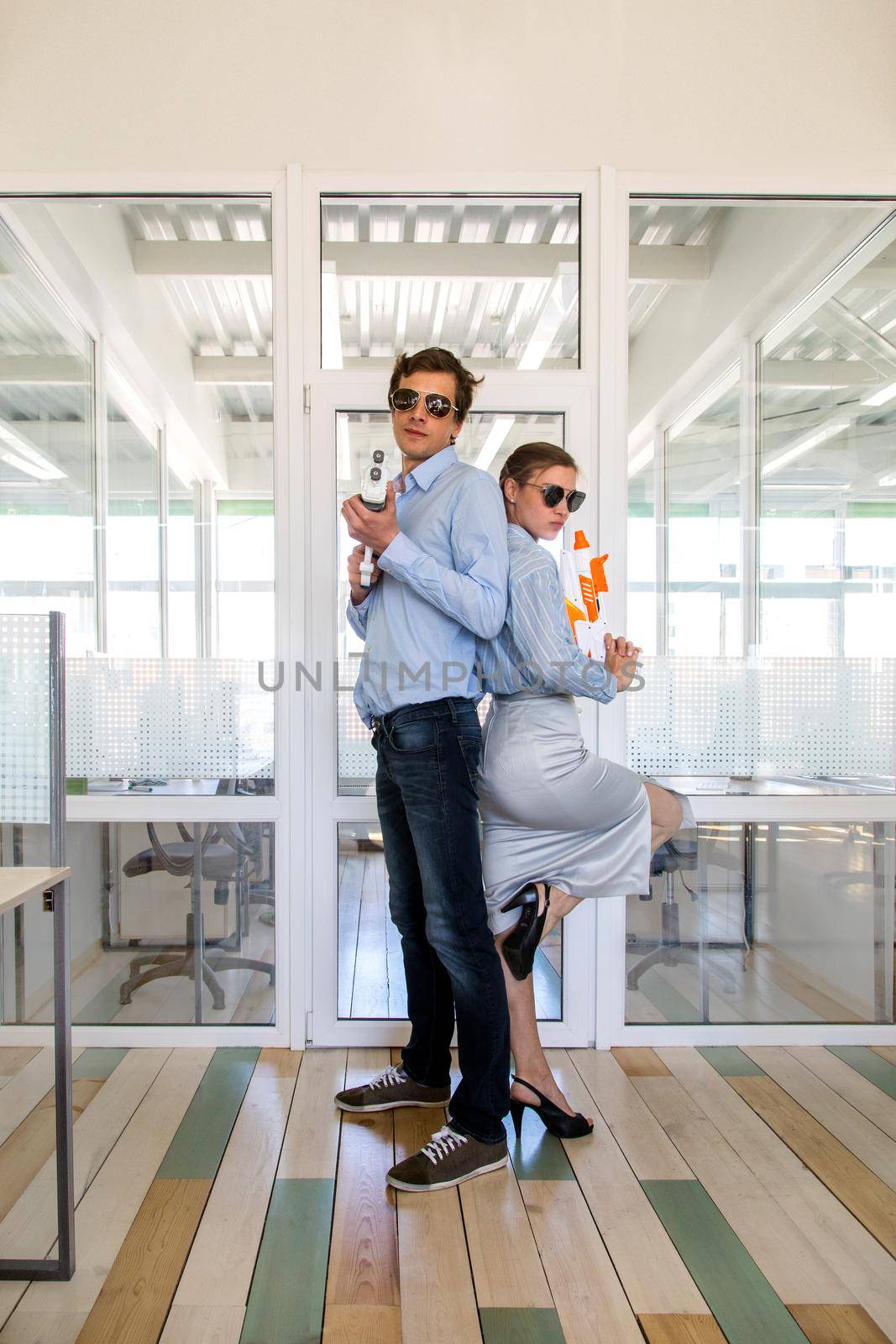 Full body side view of office workers in sunglasses standing back to back with toy pistols at workplace