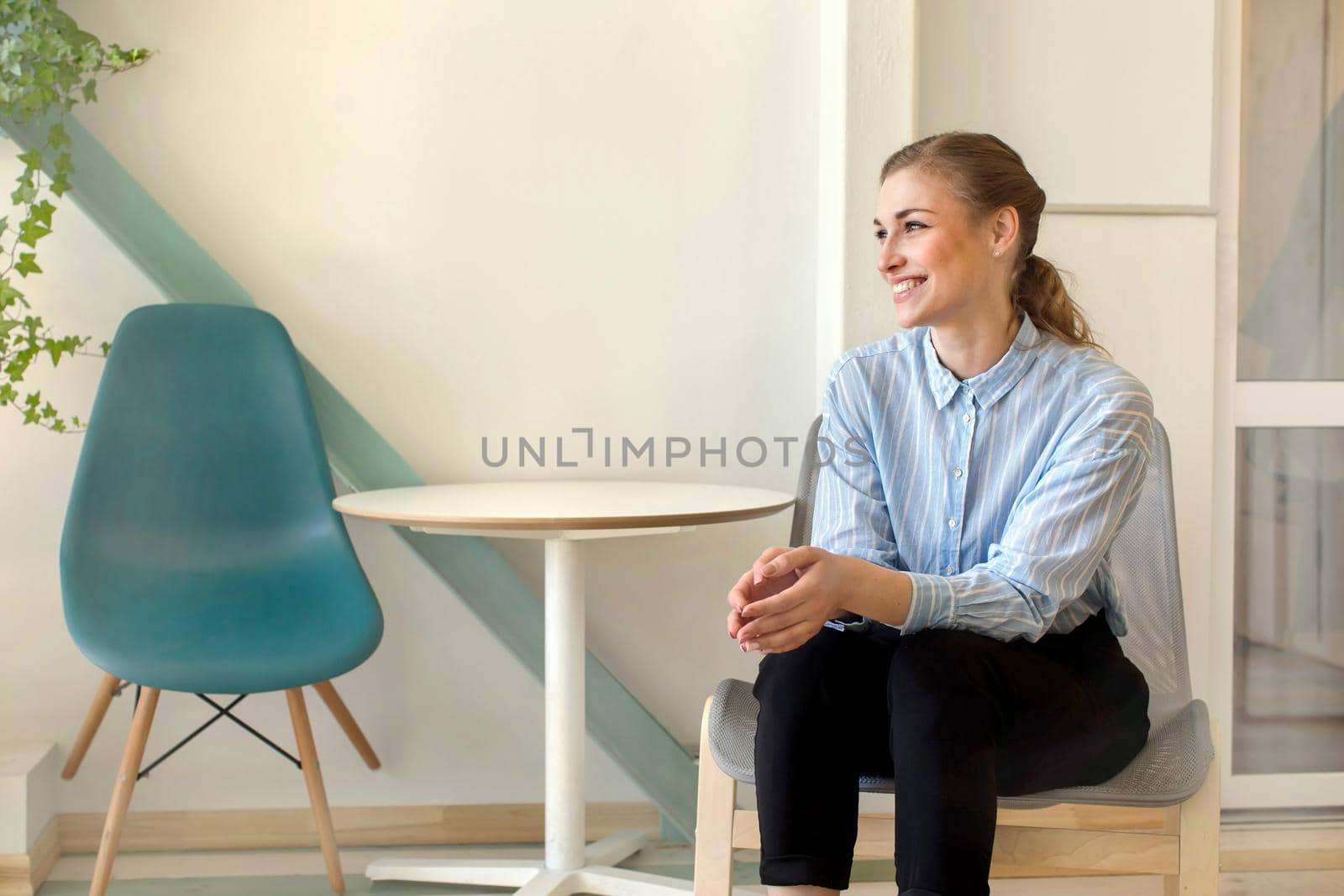 Beautiful smiling female in formal outfits sitting on chair and looking away in stylish office