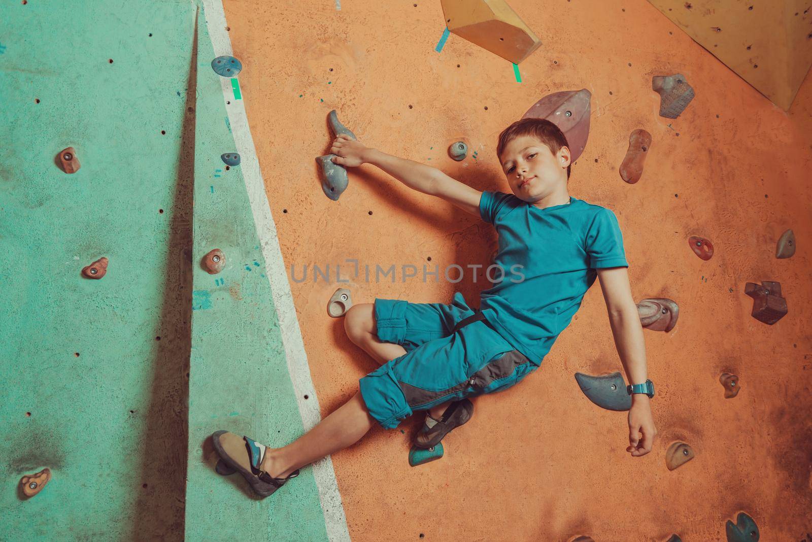 Boy climbing on artificial boulders wall in gym and looking at camera