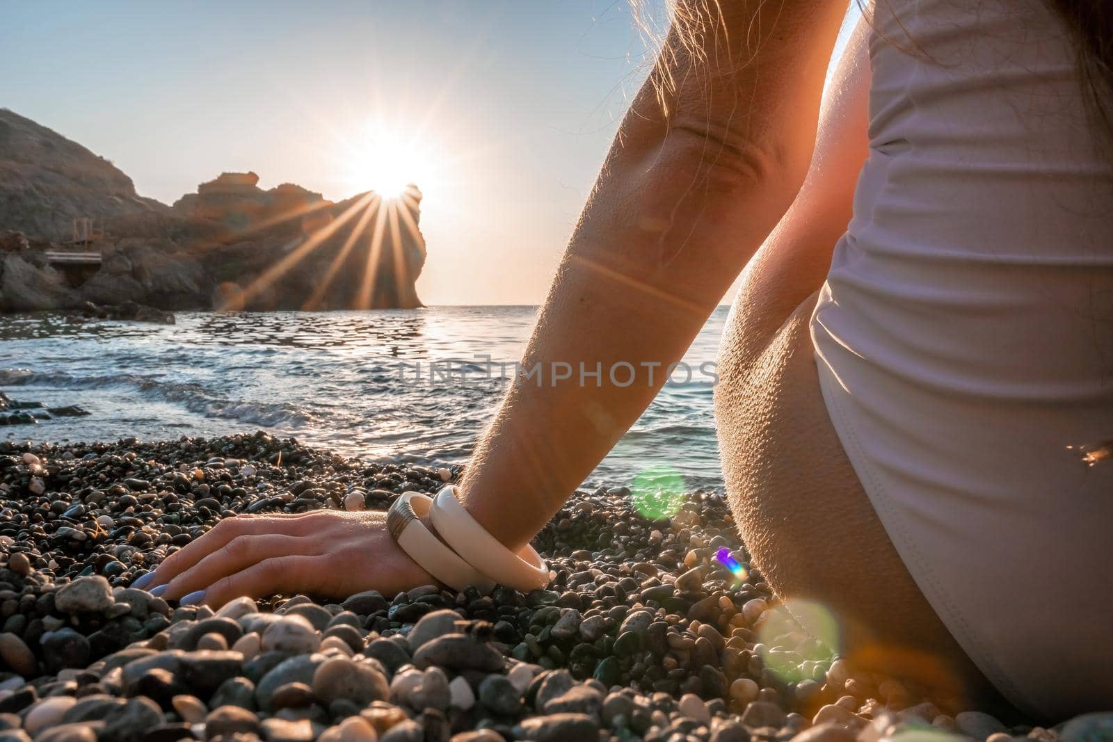 Young woman with long hair in white swimsuit and boho style braclets practicing outdoors on yoga mat by the sea on a sunset. Women's yoga fitness routine. Healthy lifestyle, harmony and meditation by panophotograph