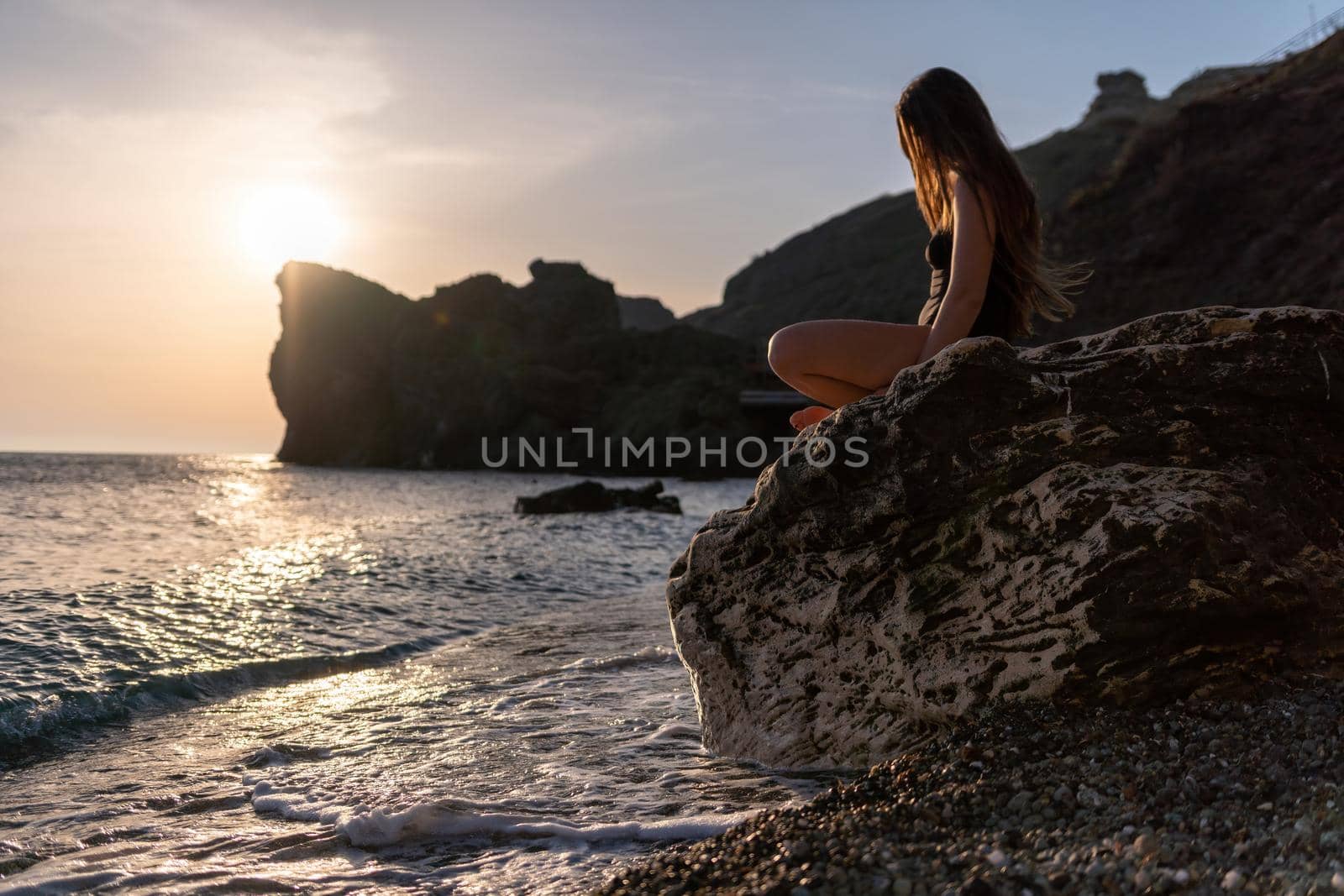 Young woman in swimsuit with long hair practicing stretching outdoors on yoga mat by the sea on a sunny day. Women's yoga fitness pilates routine. Healthy lifestyle, harmony and meditation concept.