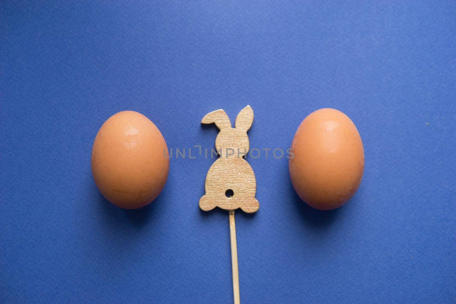 Easter background, eggs and a wooden hare on a blue background, flatlay, top view, empty space for text.
