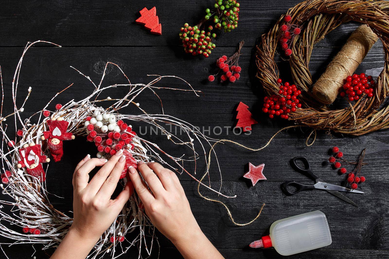 Christmas background. Top view of female hands make a Christmas wreath. Packed gifts and scrolls, spruce branches and tools on wooden table. Workplace for preparing handmade decorations.