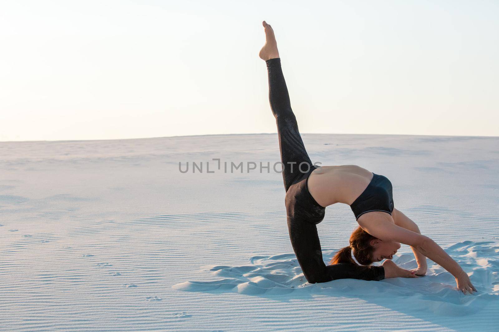Fitness yoga woman stretching on sand. Fit female athlete doing yoga pose before running training outside in amazing landscape.