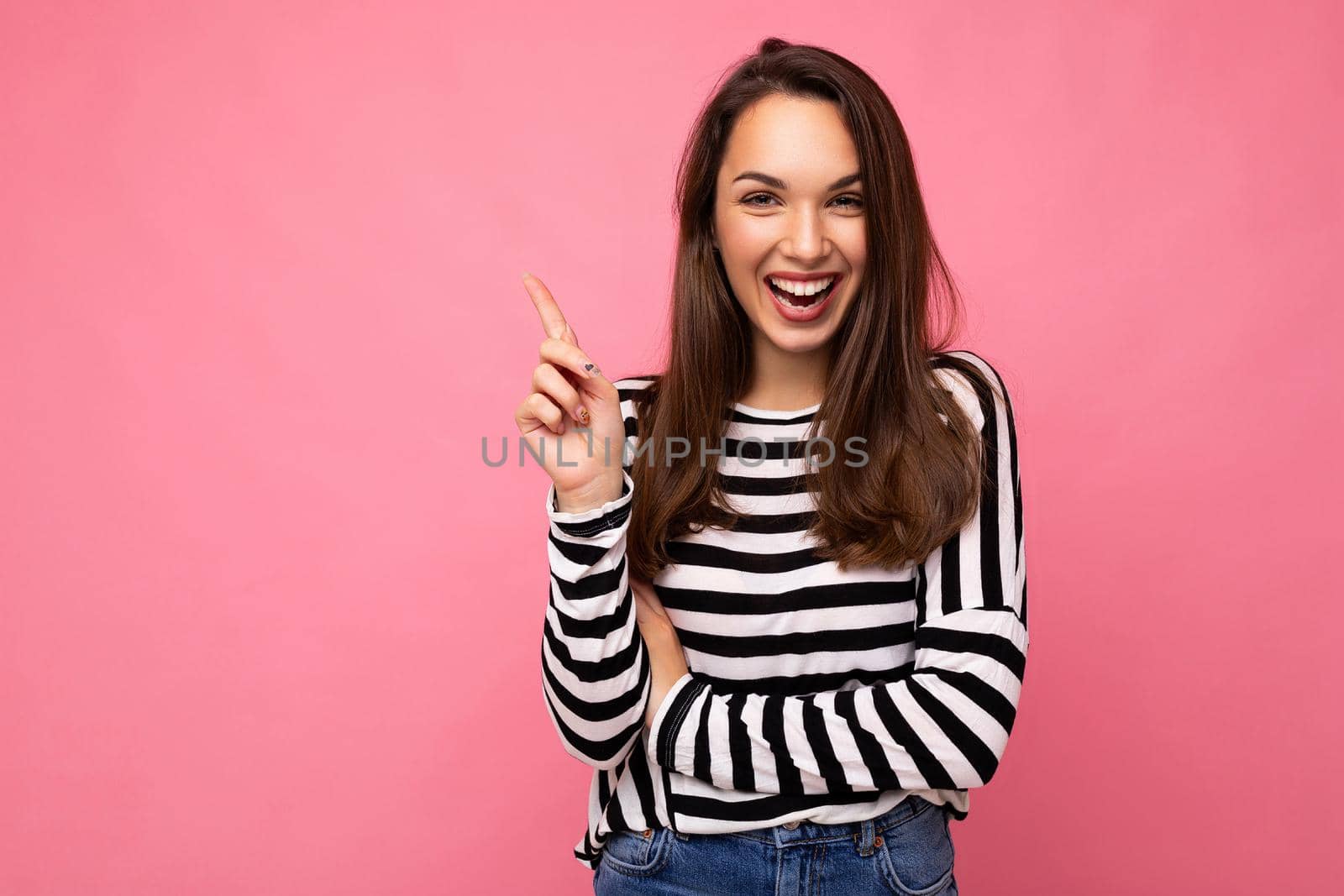 Shot of young positive happy attractive brunette woman with sincere emotions wearing casual striped longsleeve isolated on pink background with empty space and having an idea.