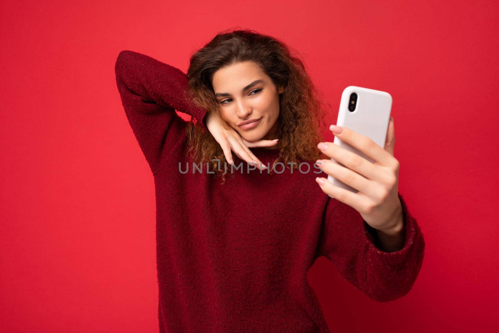Attractive charming young smiling happy woman holding and using mobile phone taking selfie wearing stylish clothes isolated over wall background.