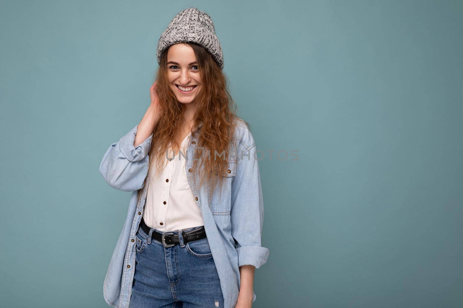Attractive smiling happy young dark blonde woman standing isolated over colorful background wall wearing everyday stylish outfit showing facial emotions looking at camera. Empty space