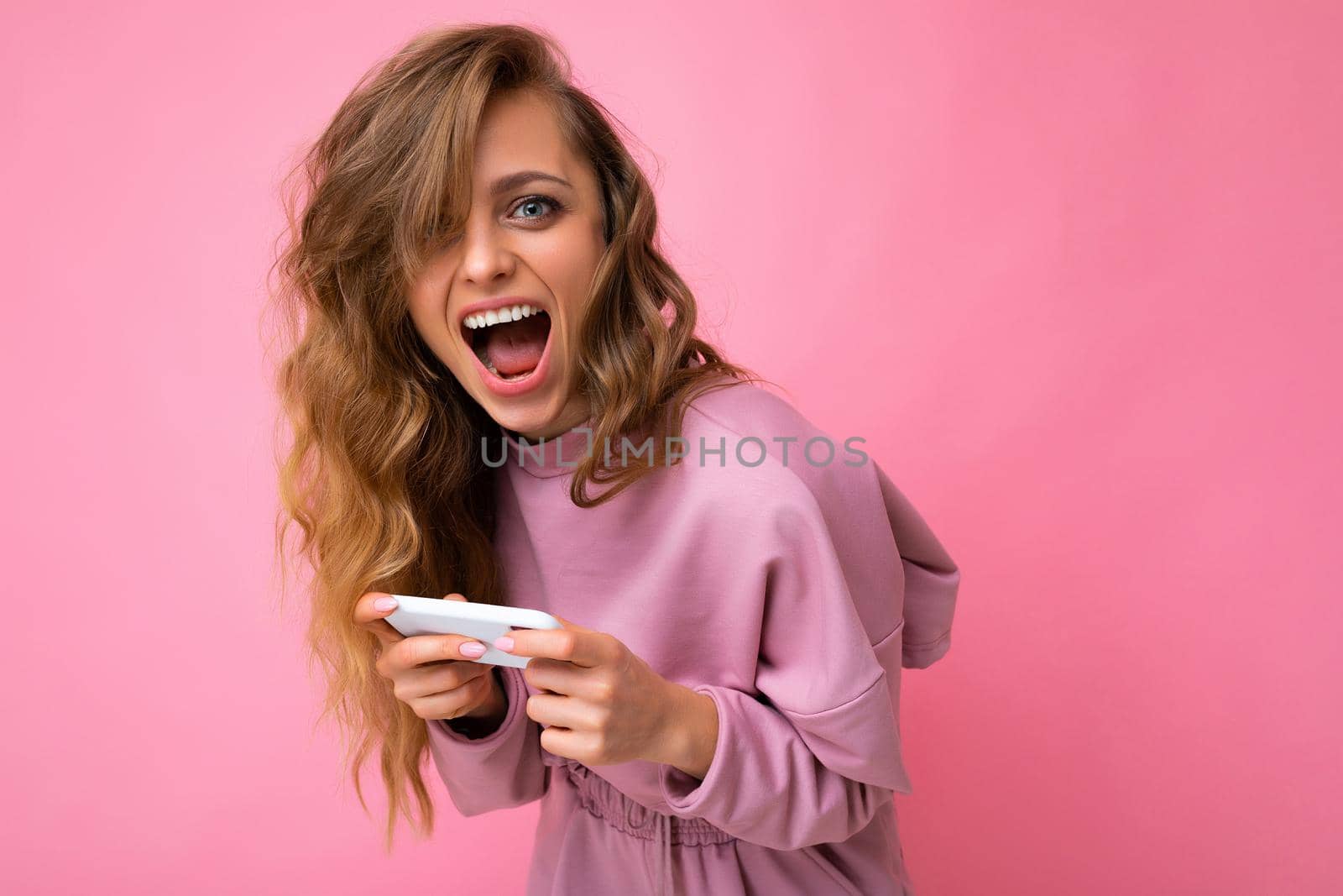 Photo of attractive crazy amazed surprised young woman wearing casual stylish clothes standing isolated over background with copy space holding and using mobile phone looking at camera.