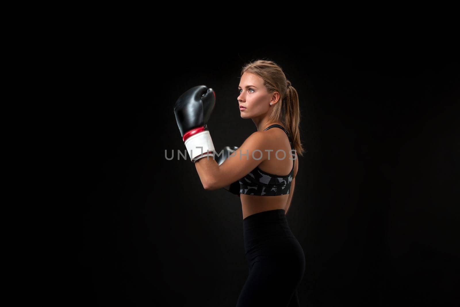 Beautiful female athlete in boxing gloves, in the studio on a black background. The boxer fulfills the blow