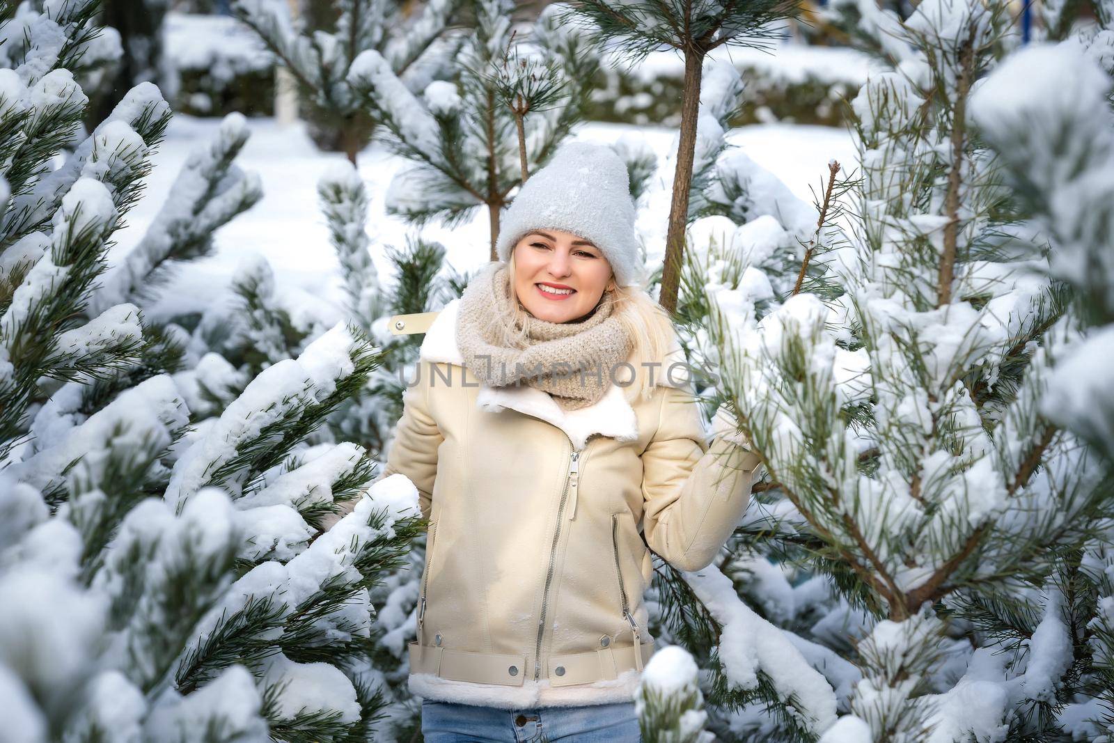 A girl in white clothes stands near a pine tree in the snow. Image with selective focus and toning.