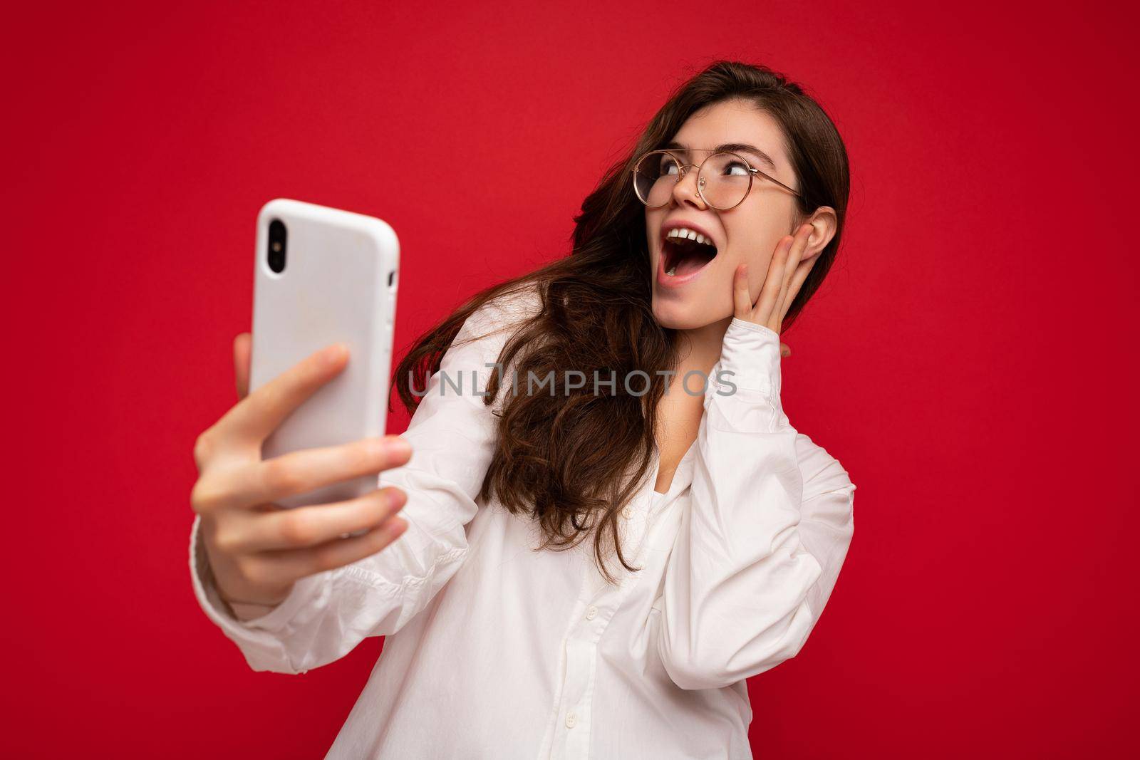 Photo of attractive crazy amazed surprised young woman wearing casual stylish clothes standing isolated over background with copy space holding and using mobile phone looking to the side.