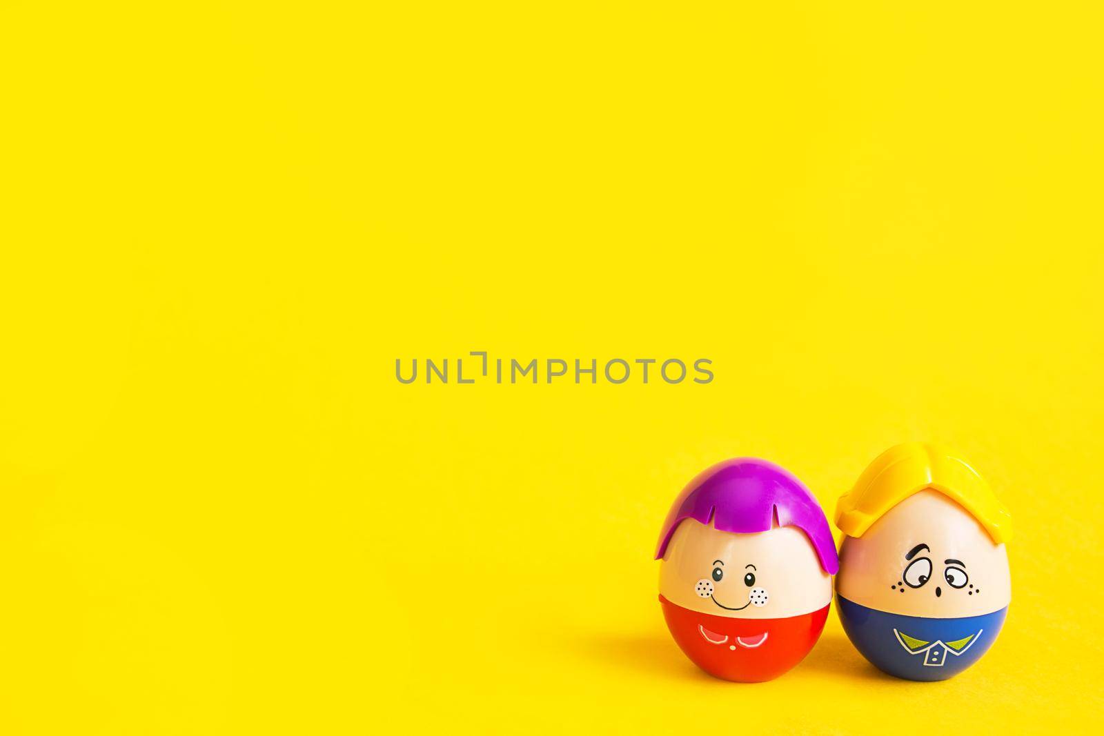 Two funny eggs boy and girl with faces on a yellow background - Easter, spring. Children's toys-a symbol of a couple of men and women, love, family. Copy space by Simol
