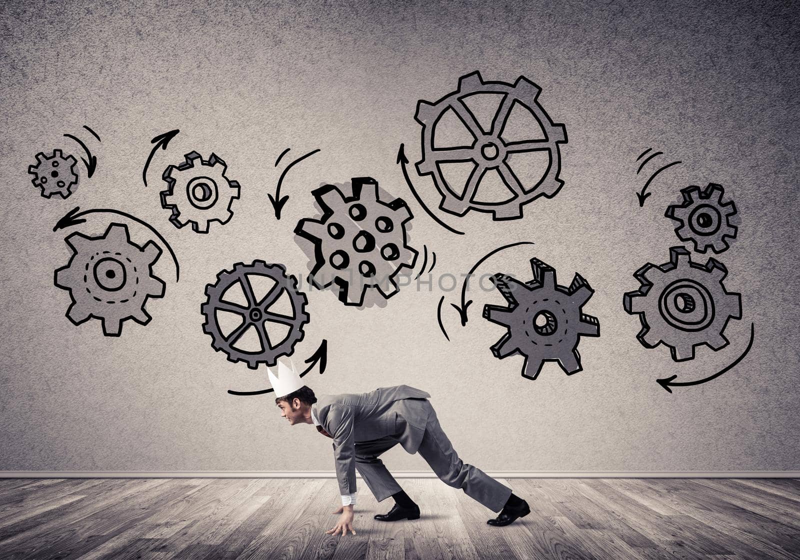 Young handsome businessman wearing white paper crown running and gear mechanism on wall