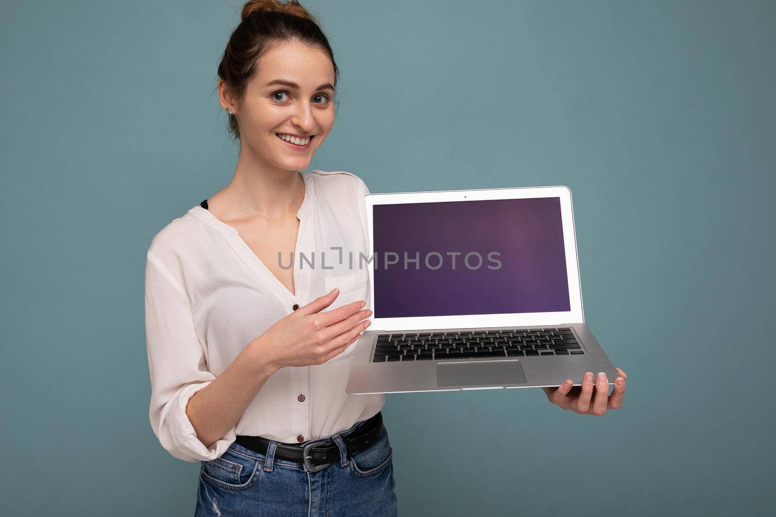 Close-up portrait of Beautiful happy young woman holding computer laptop looking at camera having fun pointing at netbook display wearing casual smart clothes isolated over wall background. Mock up, copy space