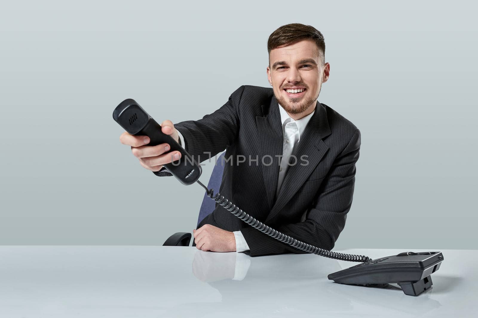 Portrait of attractive businessman holding telephone in his hand. This call is for you concept. A young man in a black suit dials the phone number while sitting in the office