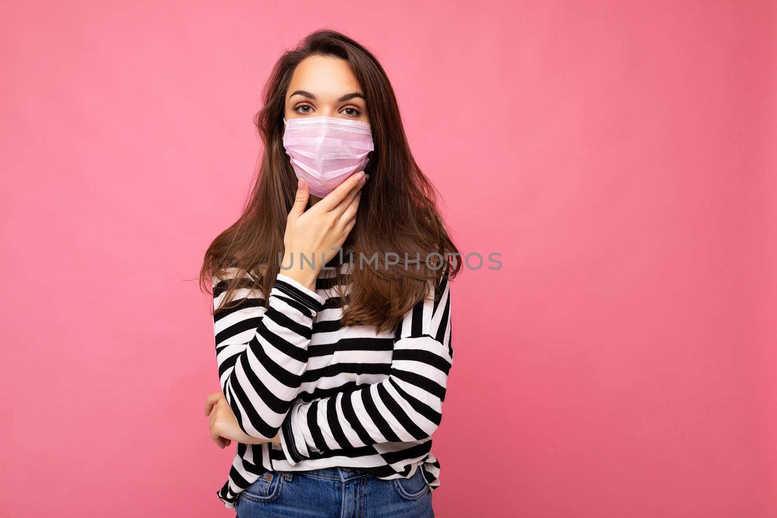 Thoughtful young beautiful woman wearing mediacal face mask isolated over background wall. Protection against COVID-19. Copy space