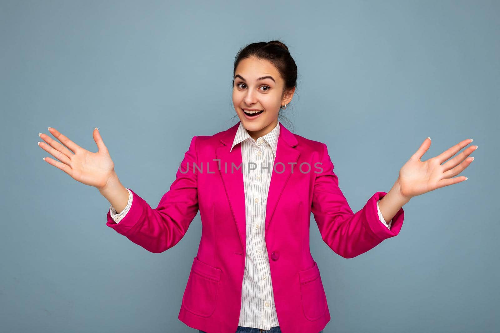 Photo portrait of young attractive beautiful positive happy delightful smiling brunette woman with sincere emotions wearing casual white shirt and stylish pink jacket isolated over blue background with copy space. Surprise and shock concept by TRMK