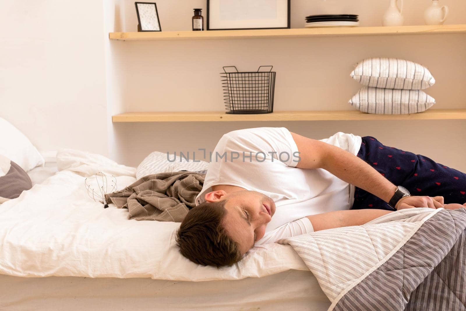 From above of tired man in nightwear lying on stylish bed and looking away during morning
