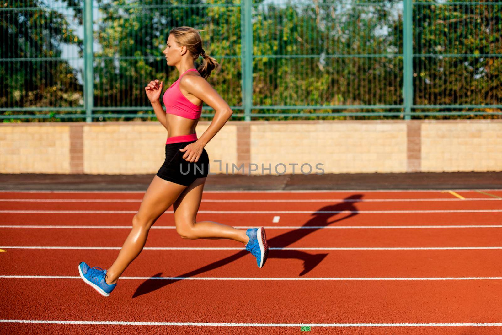 Side view beautiful young woman exercise jogging and running on athletic track on stadium. Sport, healthy lifestyle concept.