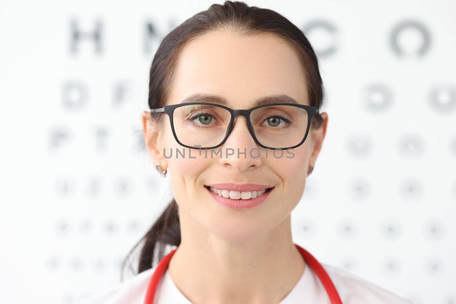 Woman ophthalmologist with glasses standing against background of table for eye test. Laser vision correction concept