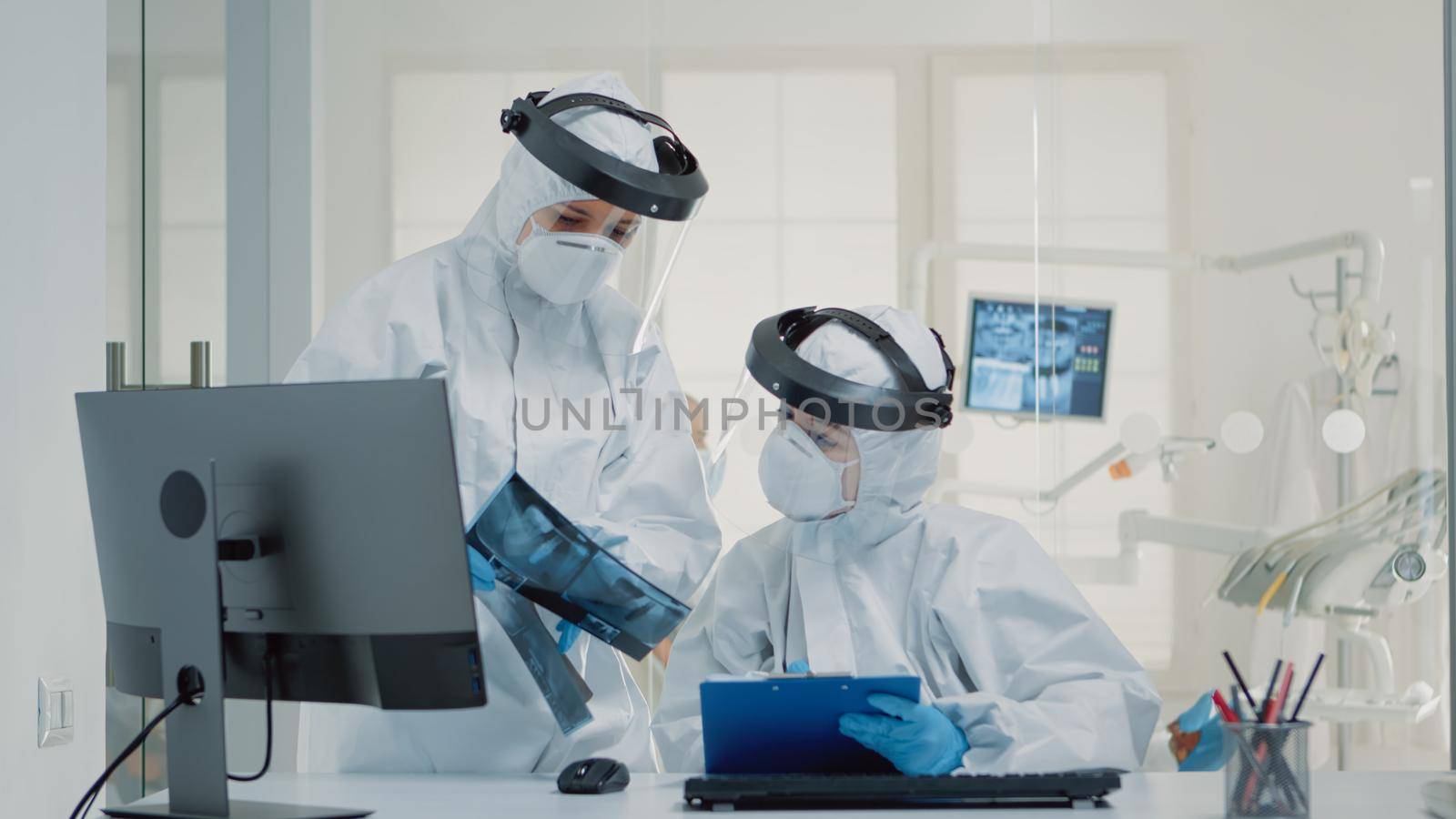 Professional dentist and assistant examining x ray of teeth while sitting in dental cabinet, during pandemic. Team of orthodontists looking at radiography scan for patient oral care