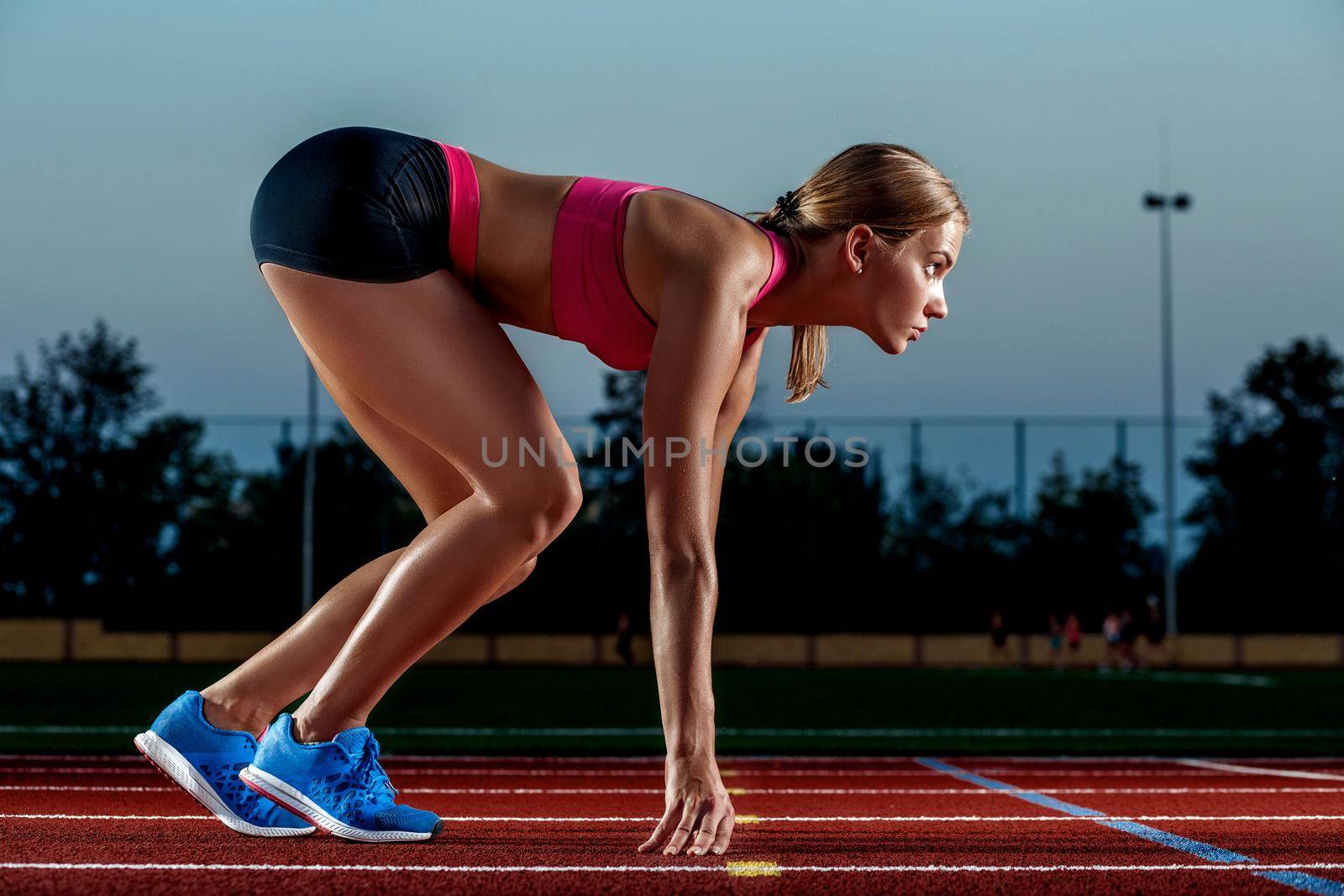 Portrait of beautiful woman ready to start running. Female athlete sprinter doing a fast sprint for competition on red lane at an outdoor field stadium.